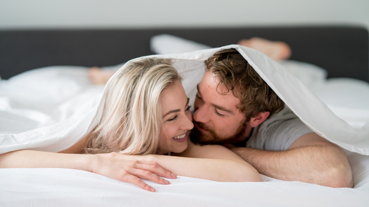 Happy couple sharing an intimate moment under bed covers together 