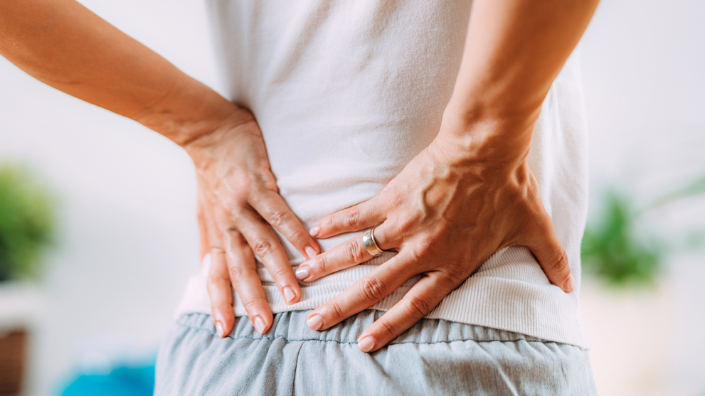 Woman holding lower back with both hands due to sciatica pain discomfort